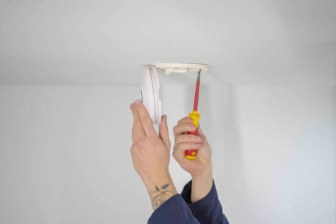 Electrician installing a photoelectric smoke alarm on a ceiling